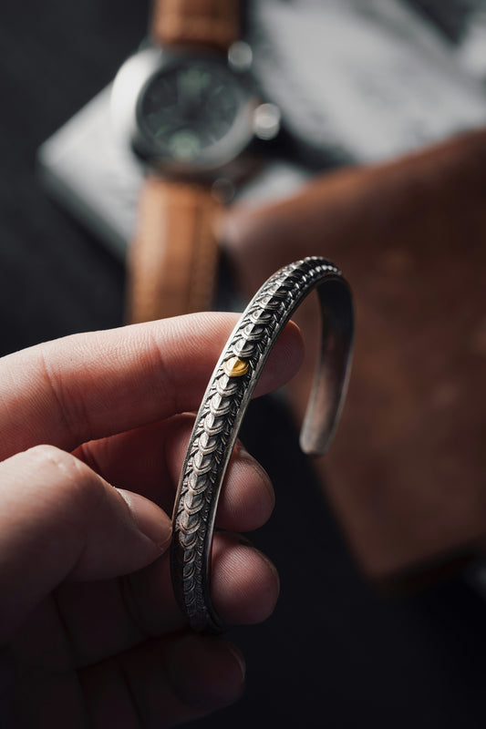 a person holding a silver bracelet with a watch in the background