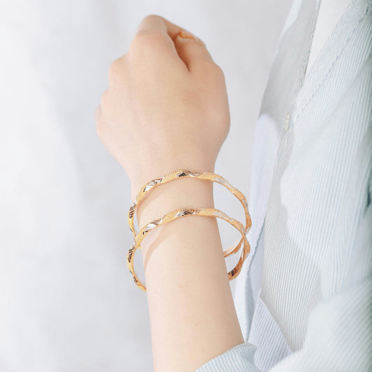 A woman's arm displays two gold bracelets.