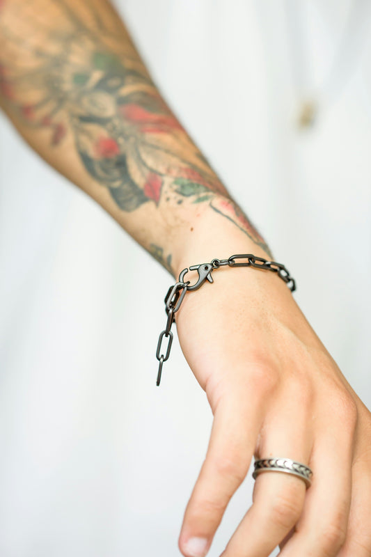 A bracelet and ring are displayed on a tattooed arm.