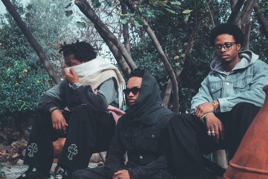 Three young men sitting outdoors in a wooded area.
