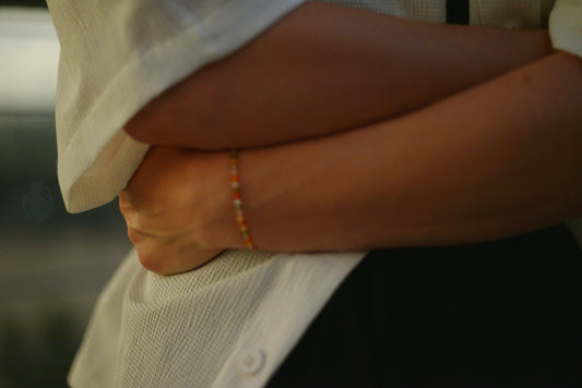 Arms crossed over torso, delicate beaded bracelet visible.