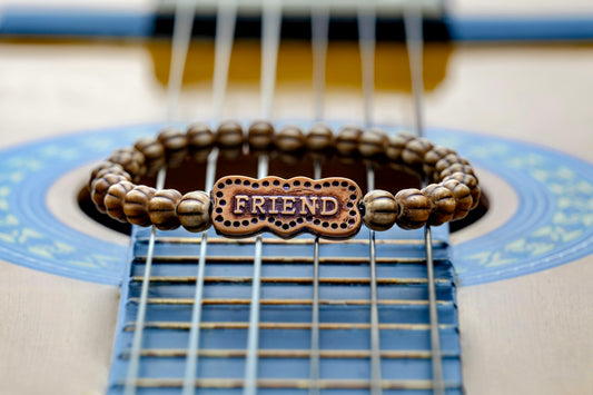 A beaded friend bracelet rests on an acoustic guitar fretboard.