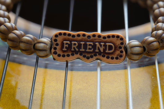 A beaded friend bracelet rests on guitar strings