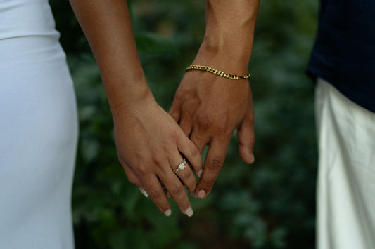 Two people holding hands, one wearing a gold bracelet and the other a ring